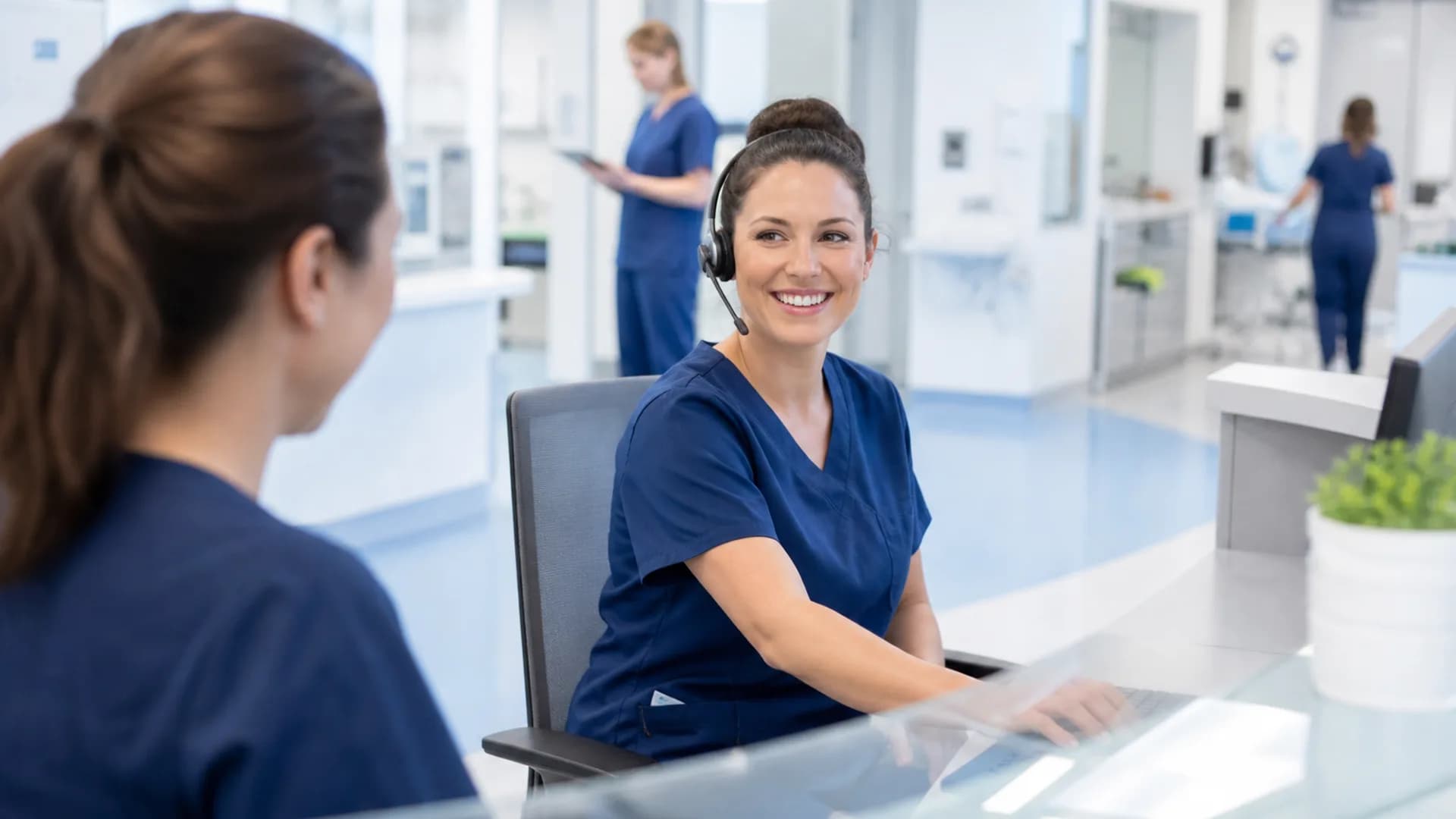 Nurse at a station desk helping a colleague